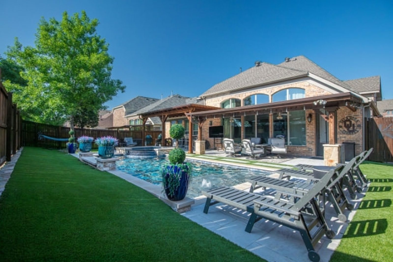 Texas outdoor living space with pool, covered patio, lounge chairs, and landscaped lawn
