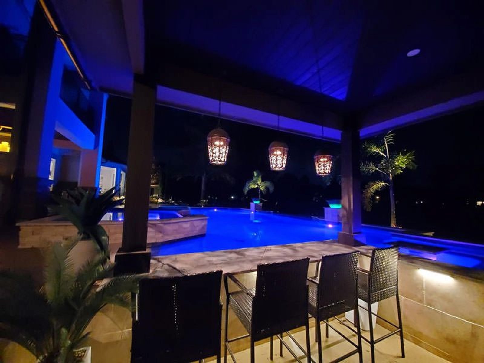 Outdoor living space featuring a glowing pool, hanging lanterns, and cozy seating under a covered patio