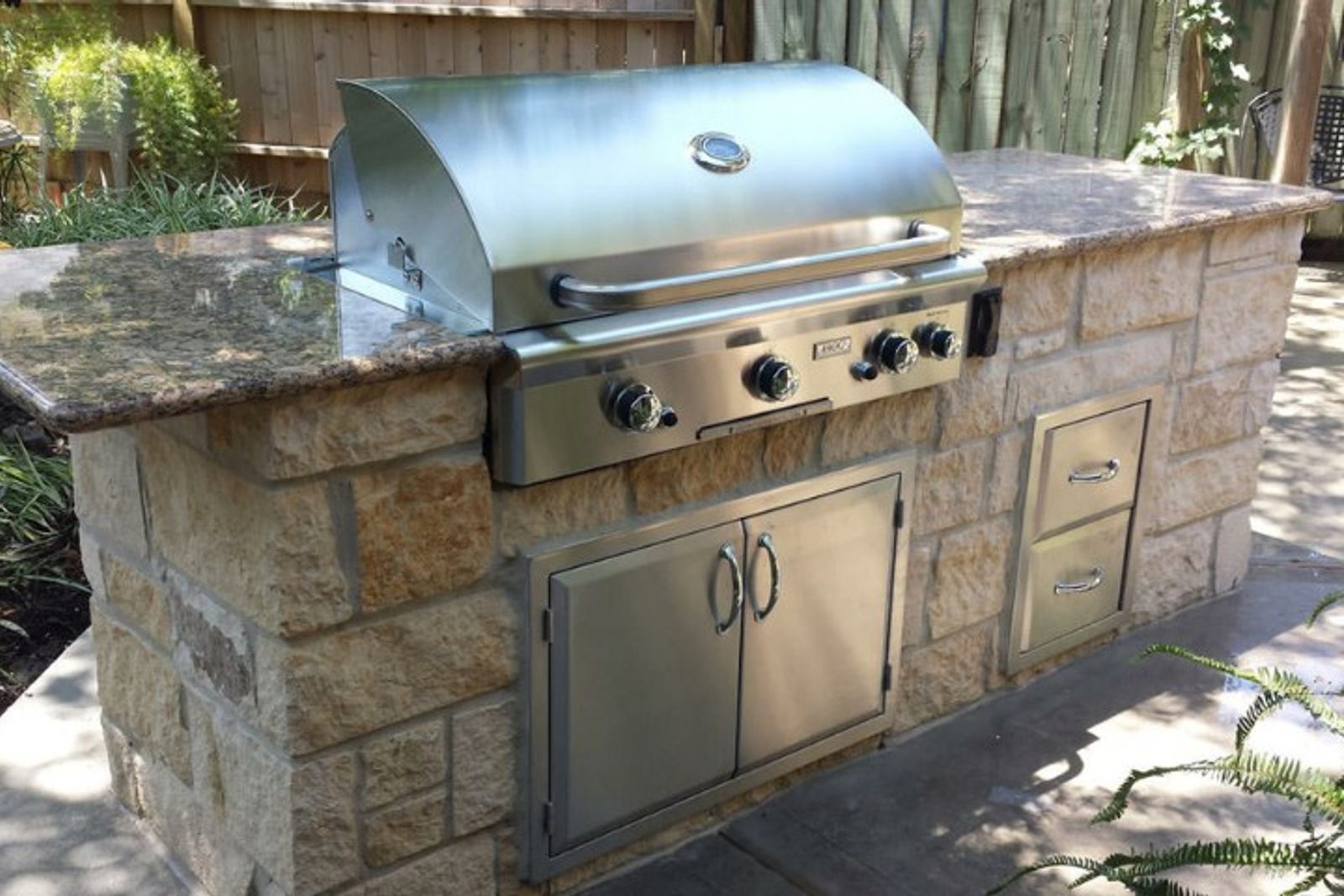 Stainless steel outdoor kitchen grill with stone countertop and built-in storage.