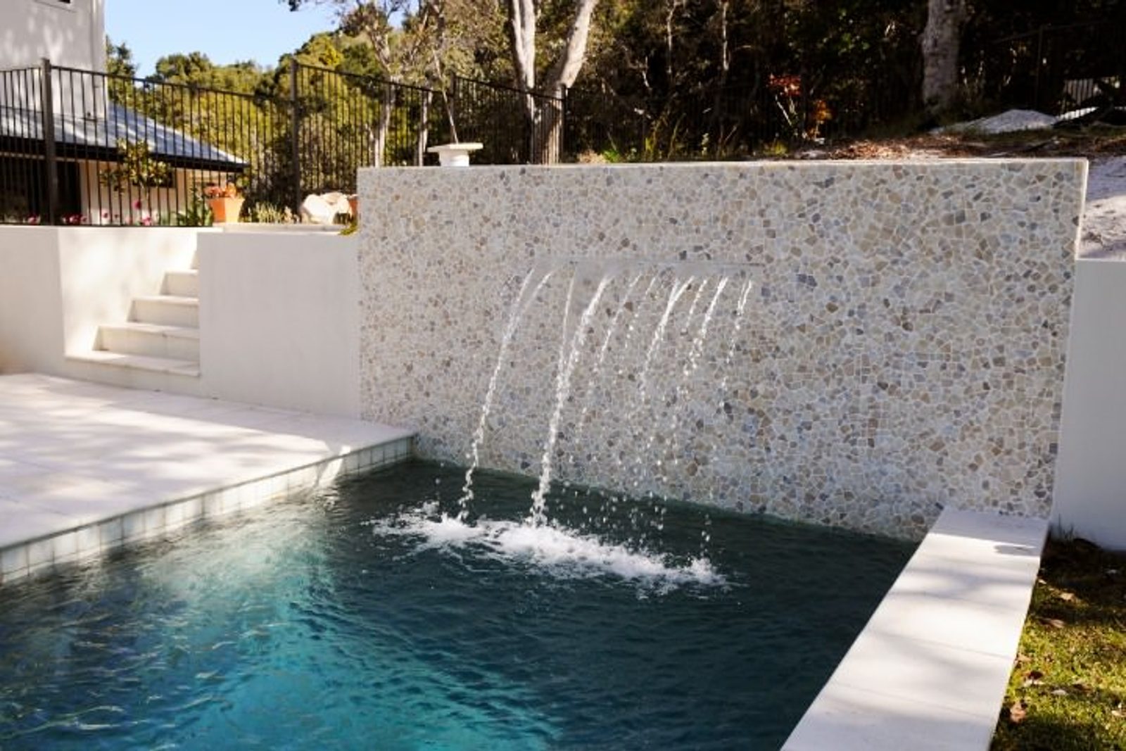 Stylish pool with a textured stone waterfall feature, adding visual appeal and tranquility to the outdoor space