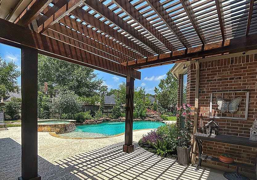 Outdoor living area with wooden pergola and landscaped pool designed by custom pool contractors in Houston