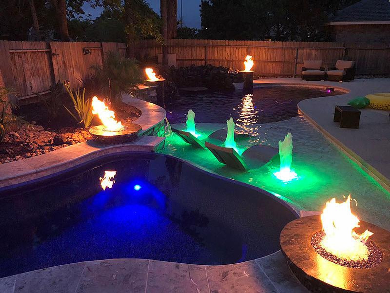 Nighttime view of a custom-designed pool with glowing fire bowls and water fountains