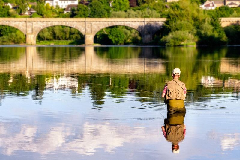 Person sat on a boat fishing with a bridge in the background