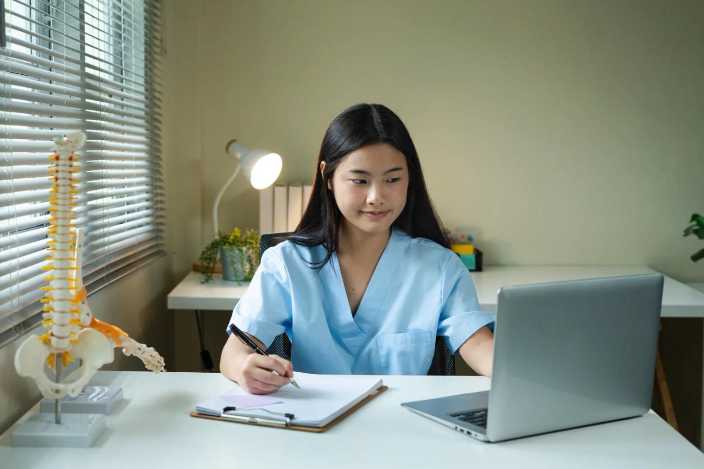 A clinician studying online coursework beside an anatomical spine model.
