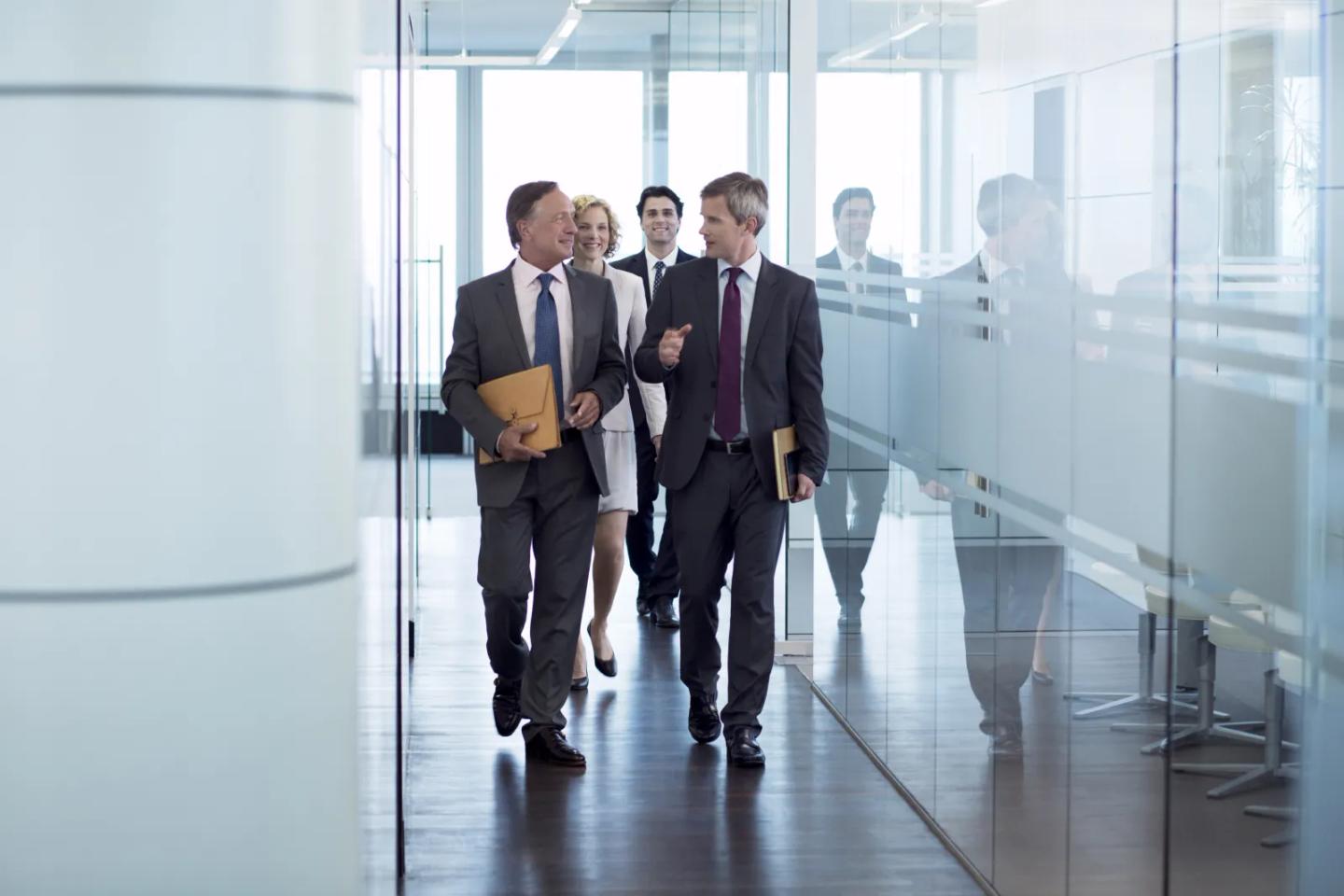 Colleagues walking together down a bright office corridor.