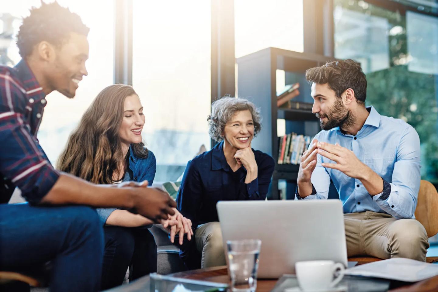 A team talking together around a laptop in a bright lounge.