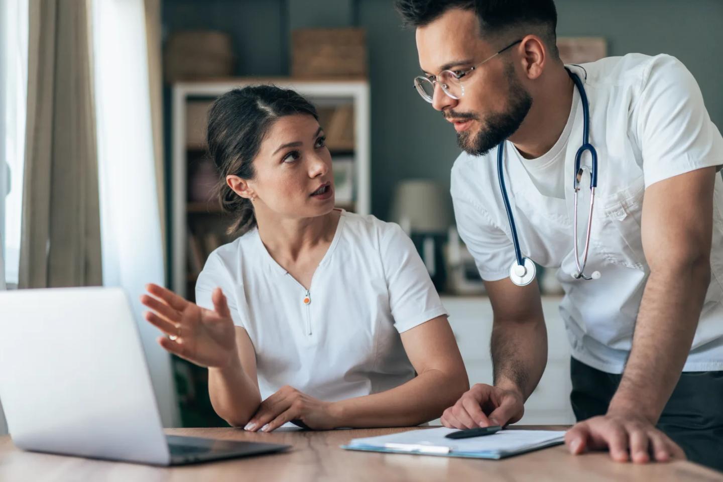 Two occupational therapy clinicians discussing a case at a laptop.