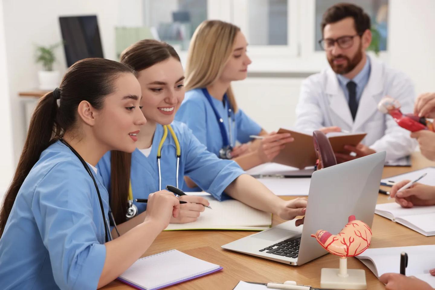 Medical students in scrubs studying together with an instructor.
