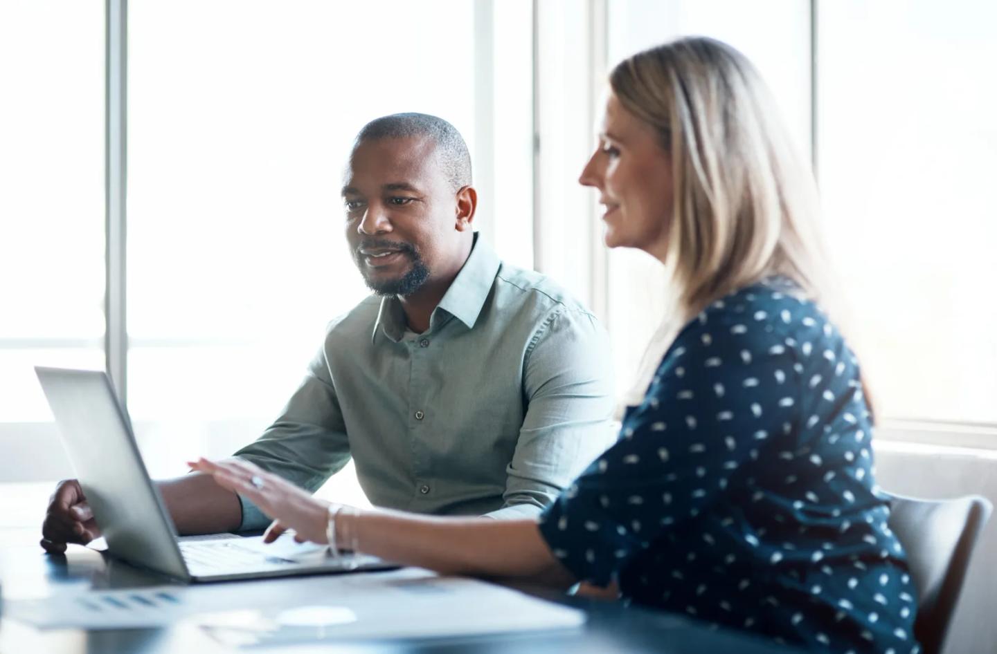 Two colleagues discussing course materials at a laptop.