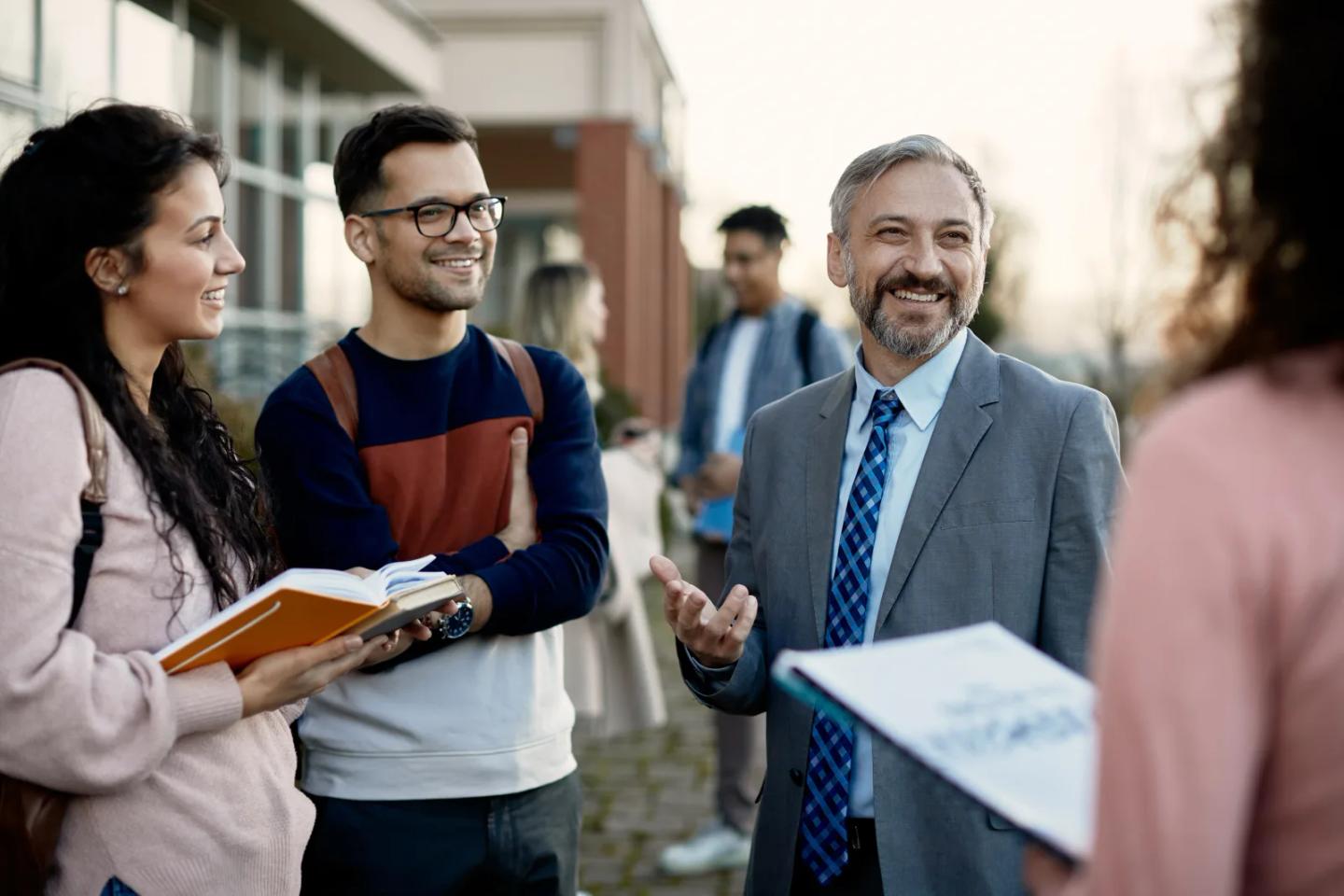 An instructor talking with students outside on campus.
