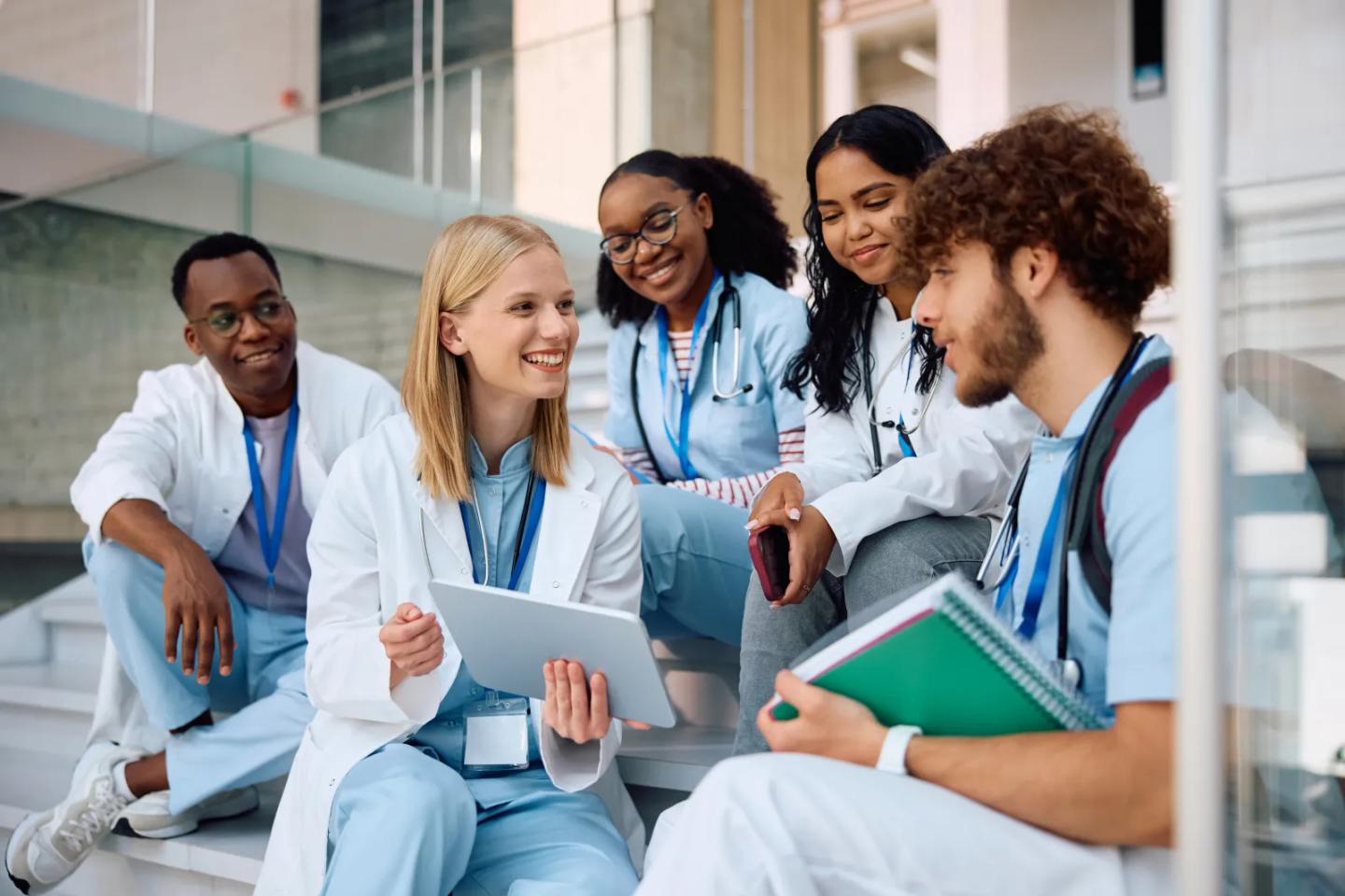 Health professions students in white coats studying together on campus steps.