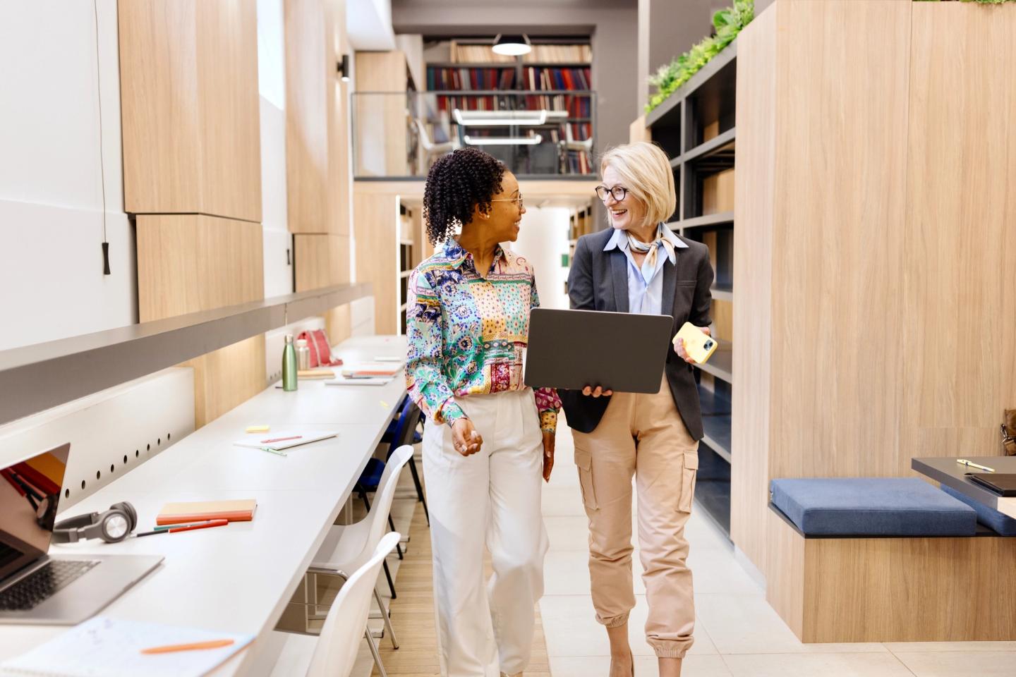 Two faculty members talking as they walk through a library.