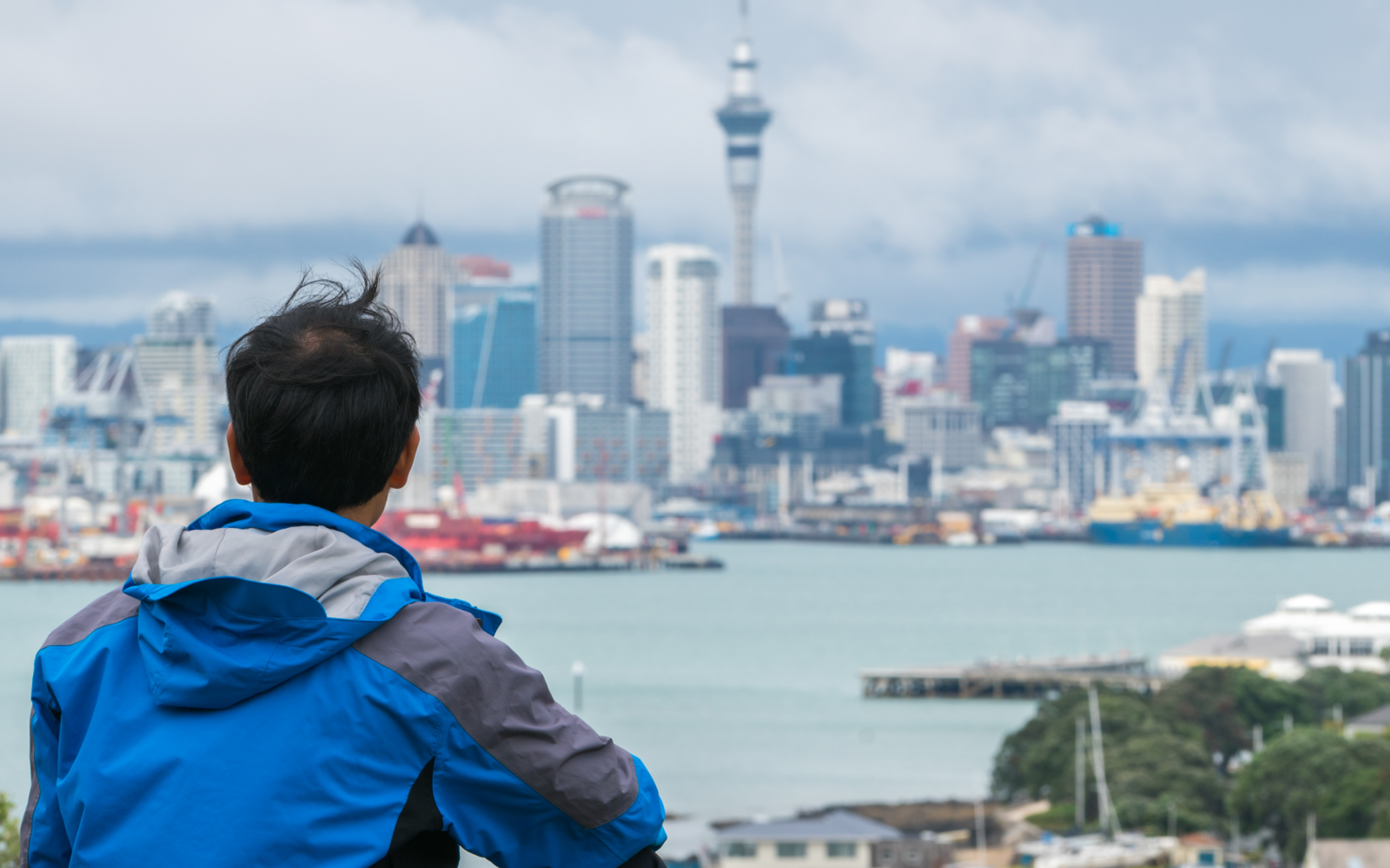 Young man sitting down on a hill and looking at Auckland city skyline