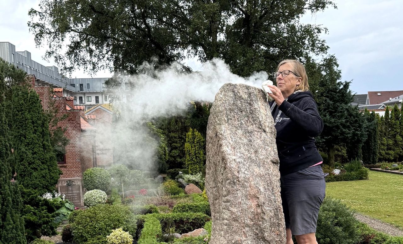 Kvindelig konservator afrenser runestenen udenfor ved Aars Kirke med damp.