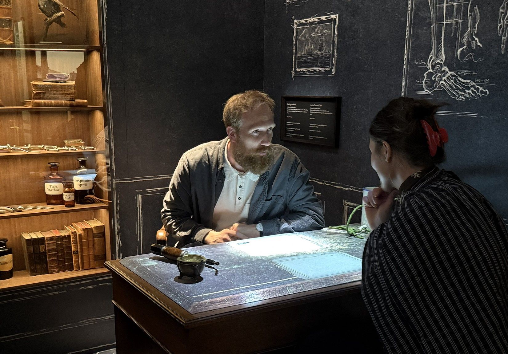 Mand og kvinde sidder over for hinanden ved et interaktivt bord i en historisk apotekerinstallation på Nationalmuseet