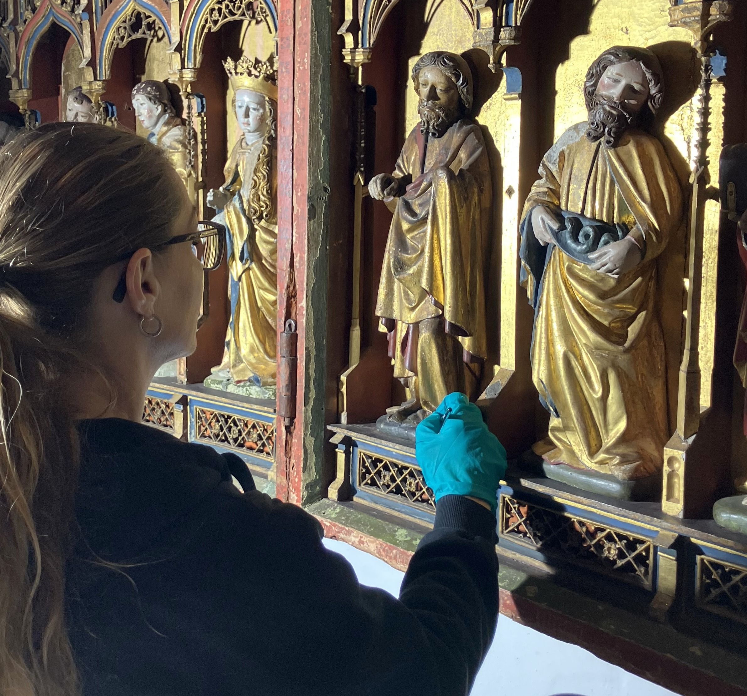 Kvindelig konservator bemaler udskårne helgenbilleder af træ, i en kirke.