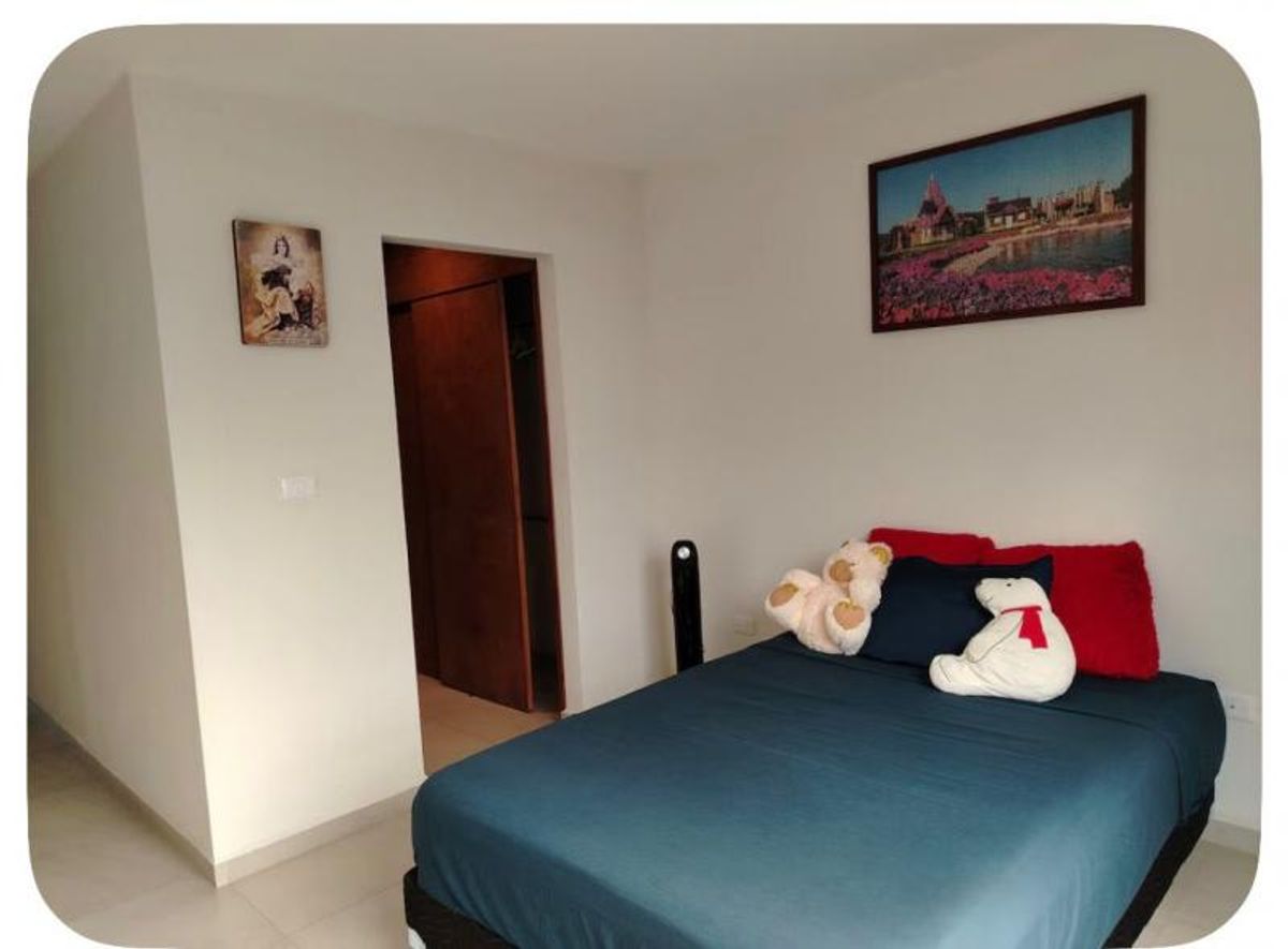 Recámara con cama vestida en azul, cojines rojos, paredes blancas y puerta de madera