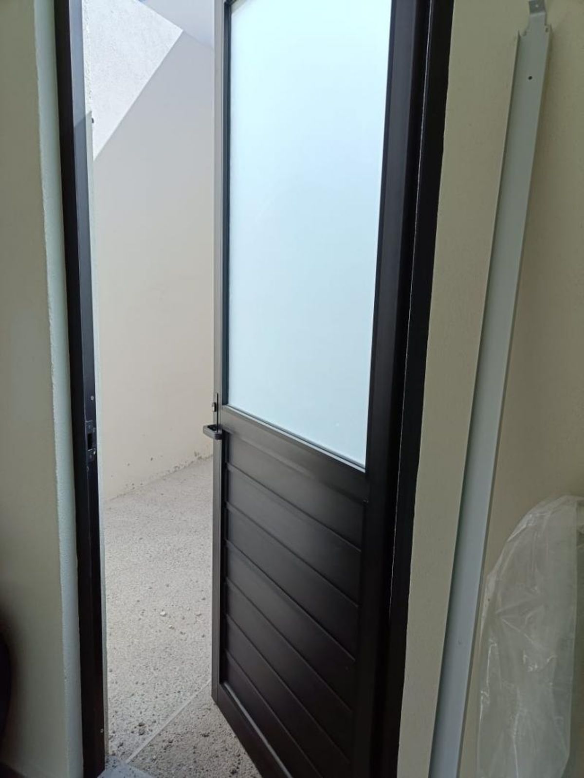 Puerta de aluminio negro con vidrio esmerilado abierta hacia patio exterior de piso claro