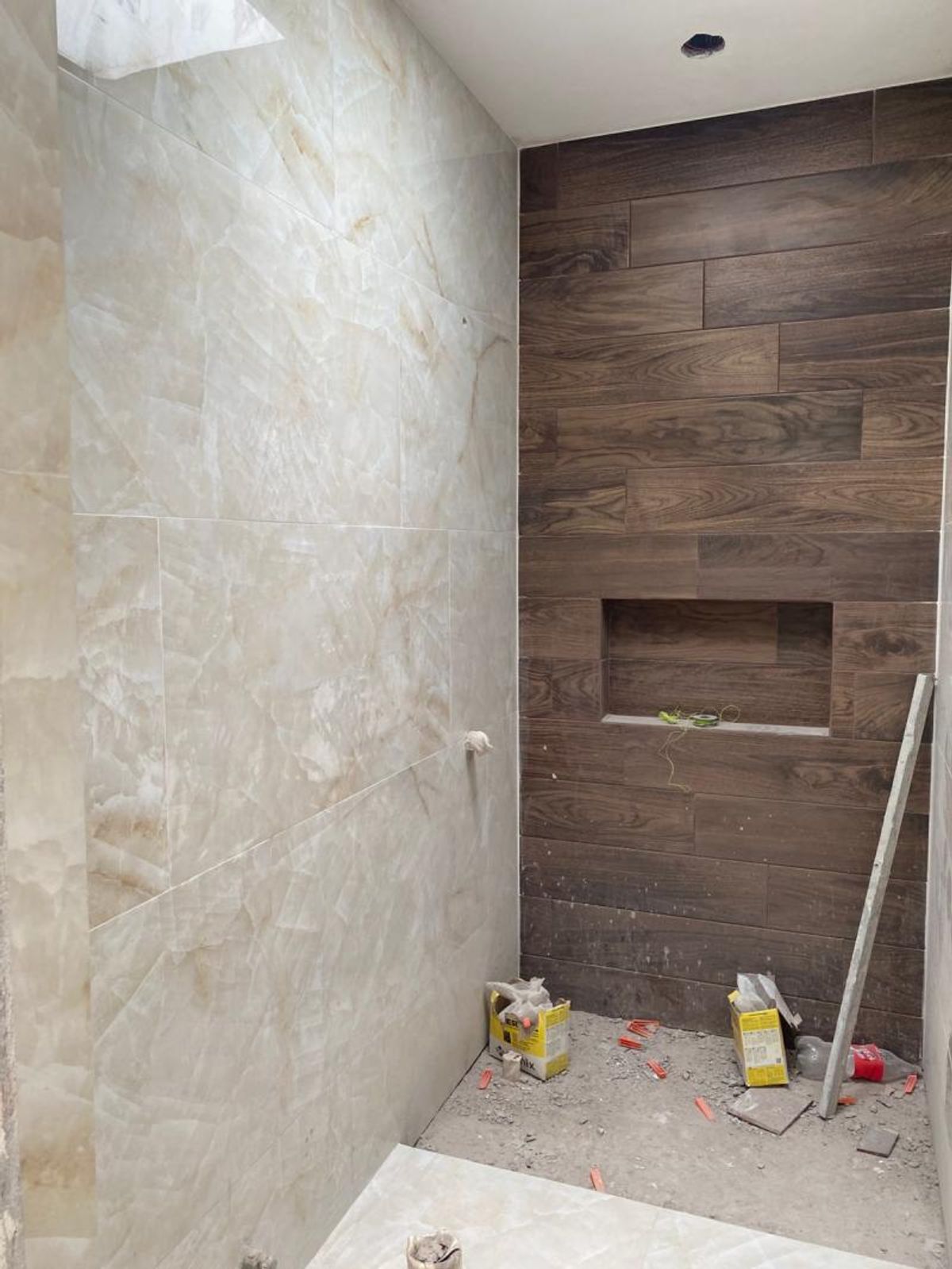 Área de ducha con azulejos tipo madera, nicho empotrado y revestimiento estilo mármol claro