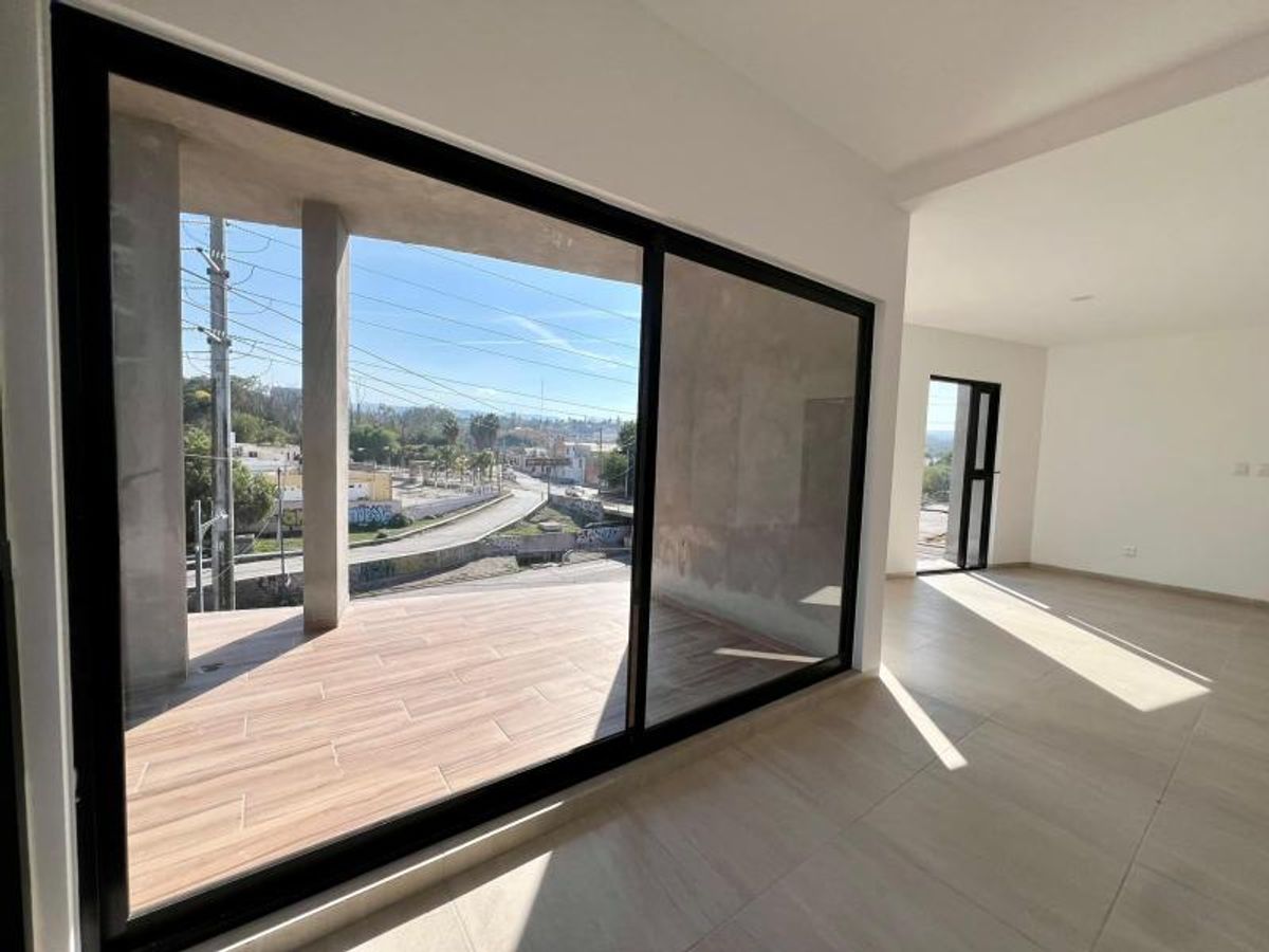 Interior con piso claro y ventanal de marco negro hacia terraza con piso tipo madera