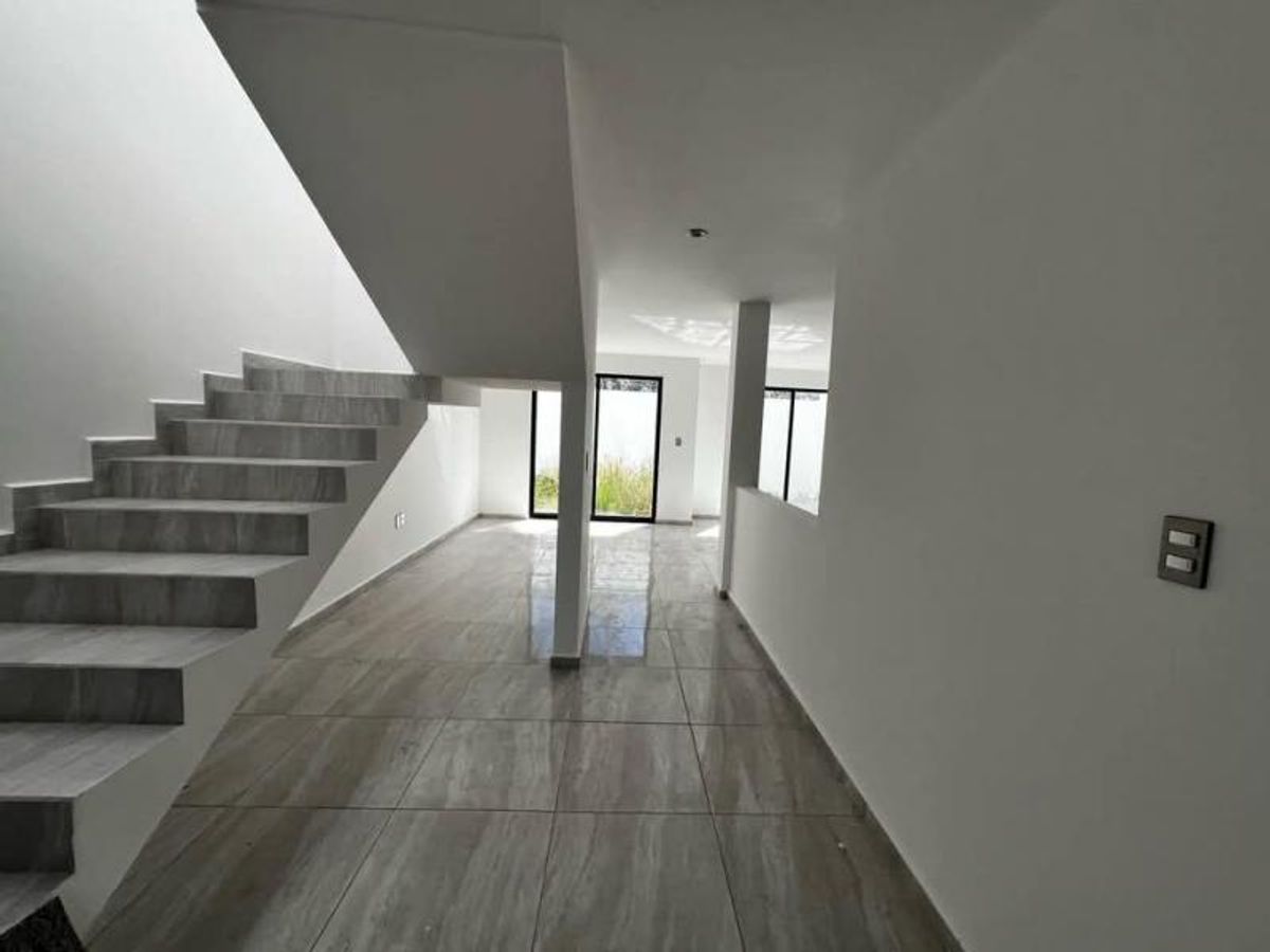 Pisos de porcelanato brillante, paredes blancas, escalera gris y ventanales de cristal al fondo