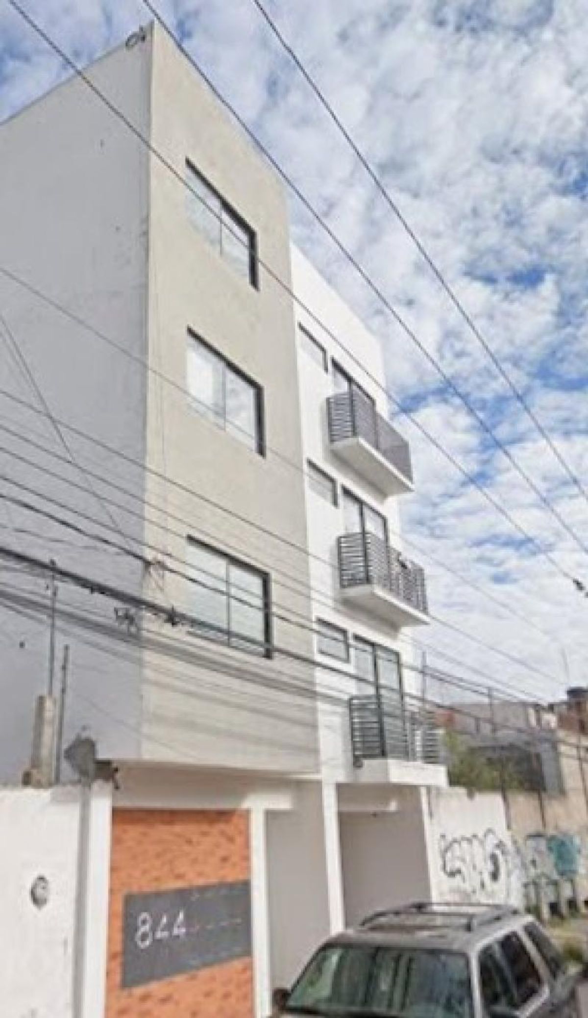 Edificio de departamentos con fachada blanca y beige, balcones metálicos negros y ventanales rectangulares