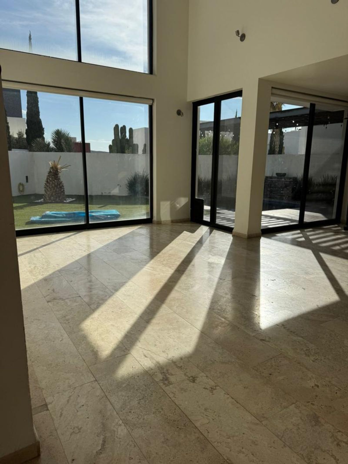 Interior con piso de mármol beige, ventanales de piso a techo y luz natural