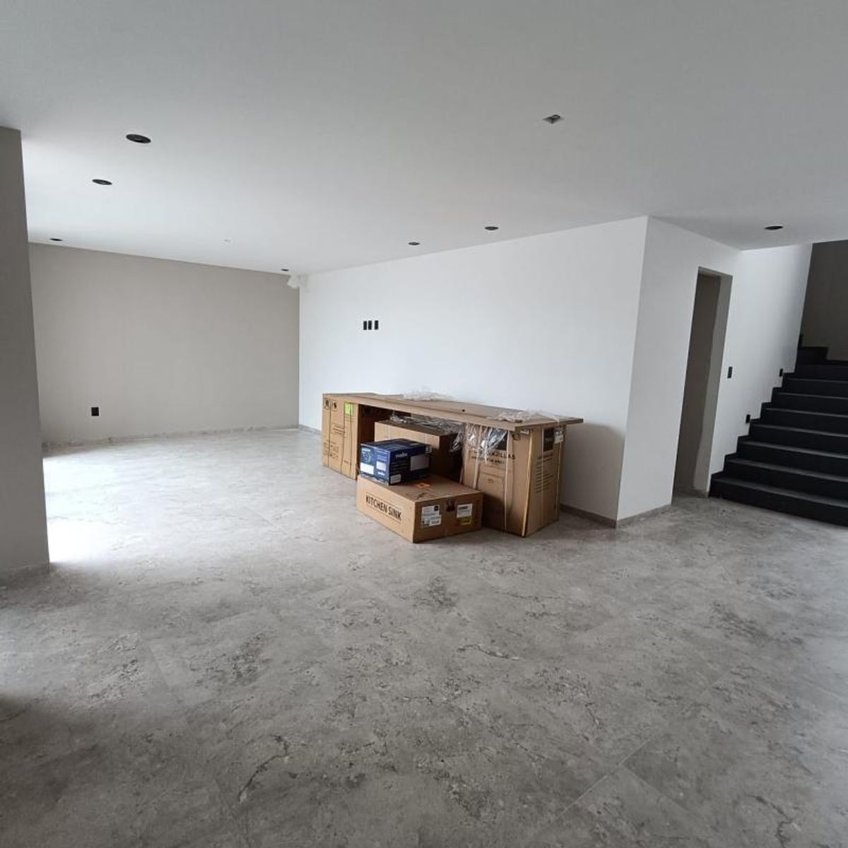 Interior de planta baja con piso de porcelanato gris, paredes blancas y escaleras negras