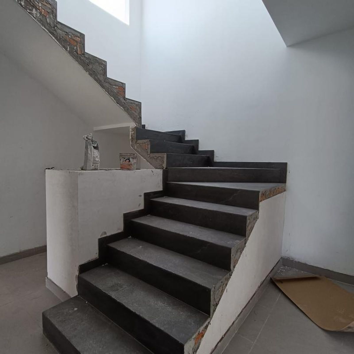 Escalera interior con escalones de piedra negra, paredes blancas y piso gris