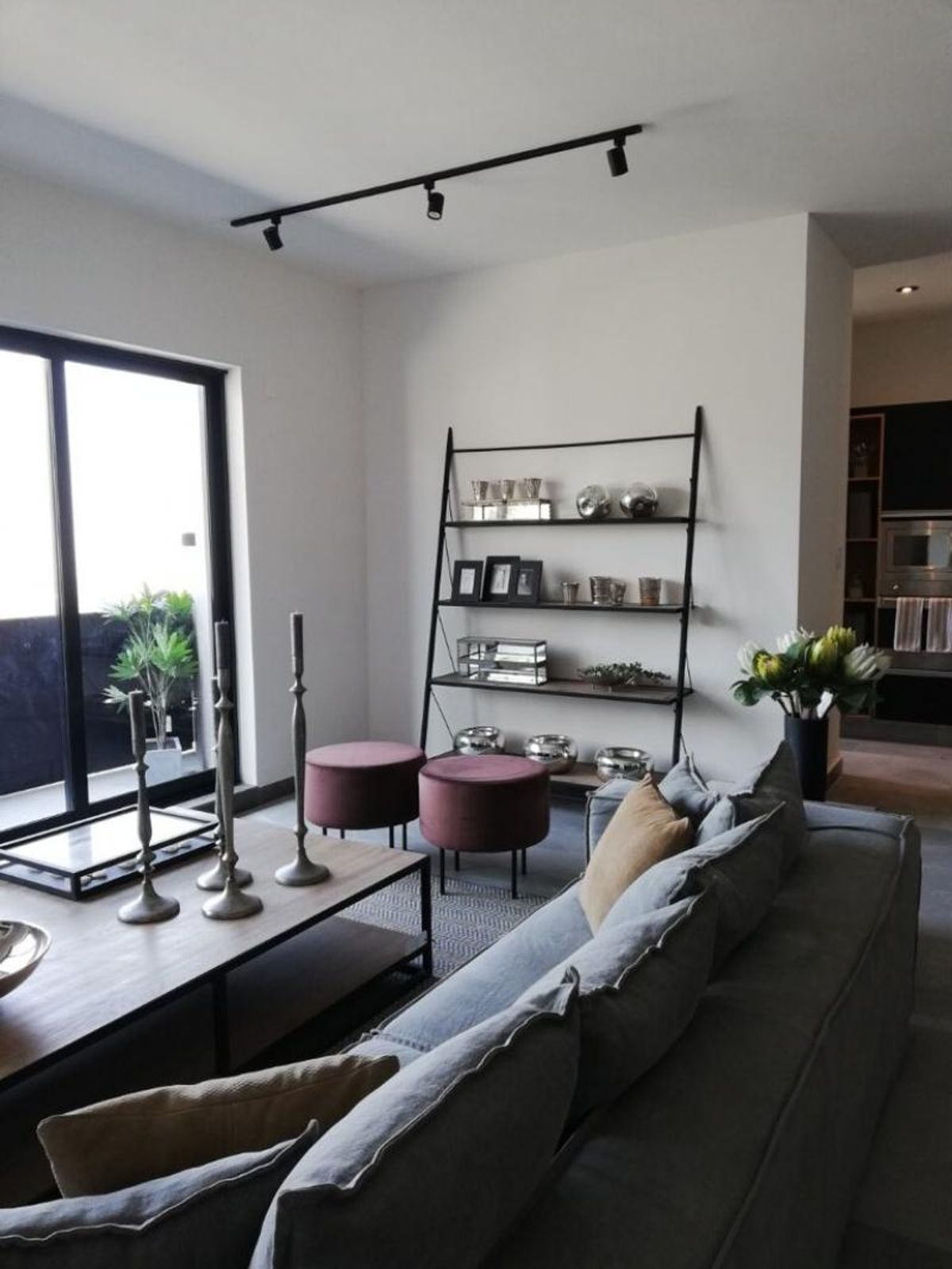 Sala con sofá gris, mesa de madera, pufs de terciopelo rosa y estantería metálica