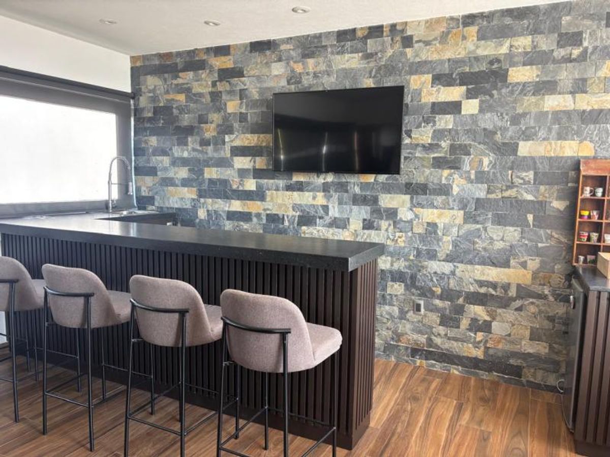 Barra de bar con cuatro bancos beige, pared de piedra decorativa y televisión empotrada