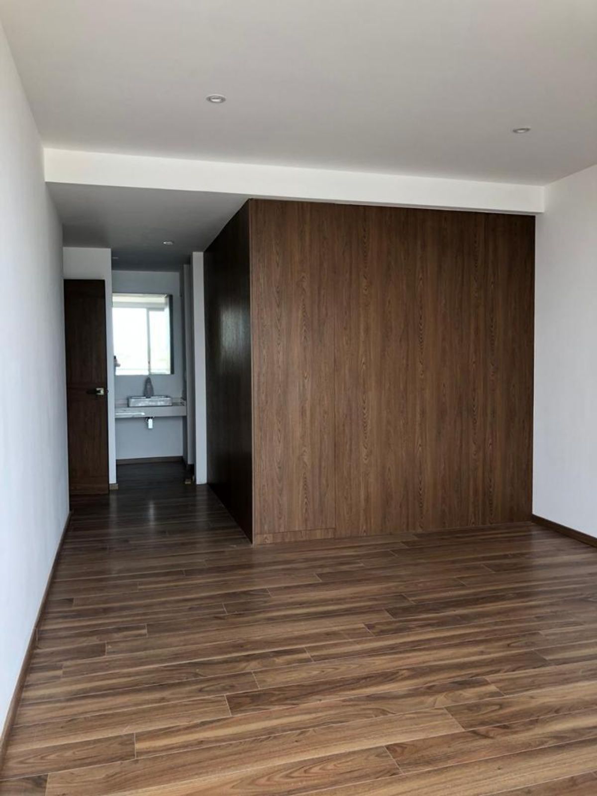 Habitación vacía con piso de madera laminada, muro de madera y baño al fondo