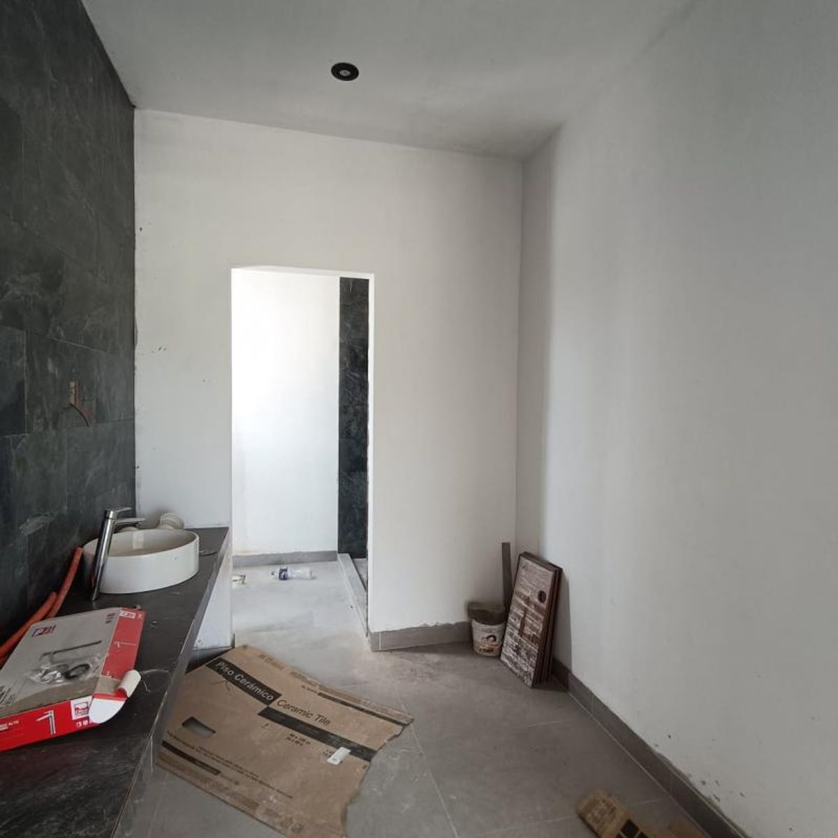 Baño en construcción con lavabo de sobreponer blanco y pared revestida en azulejo oscuro