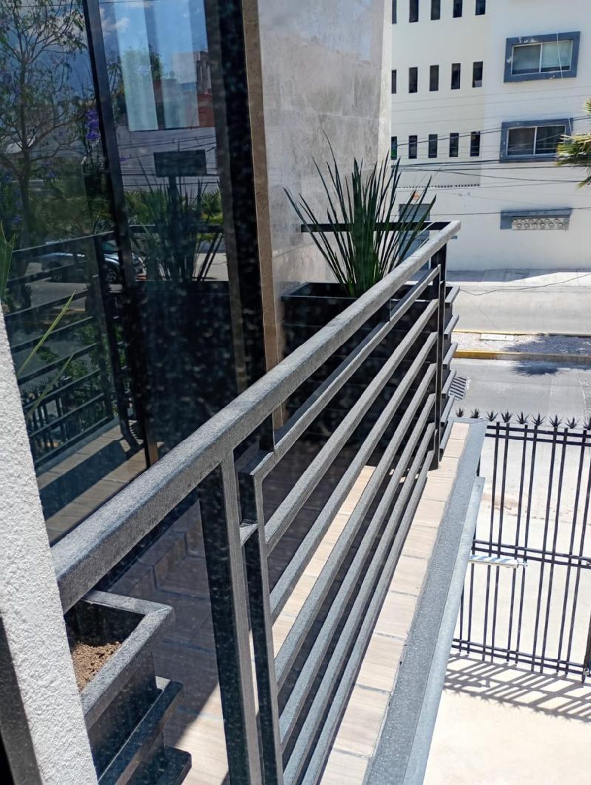 Balcón con barandal de metal negro, macetero con agaves y ventanal de cristal
