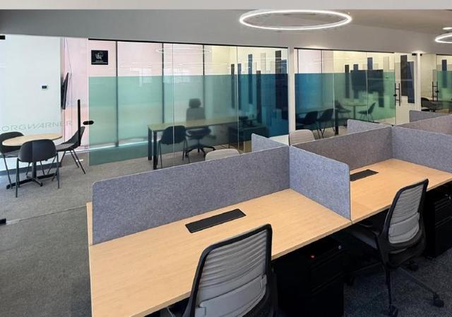 Oficina con escritorios de madera, divisores grises, sillas de trabajo y divisiones de cristal