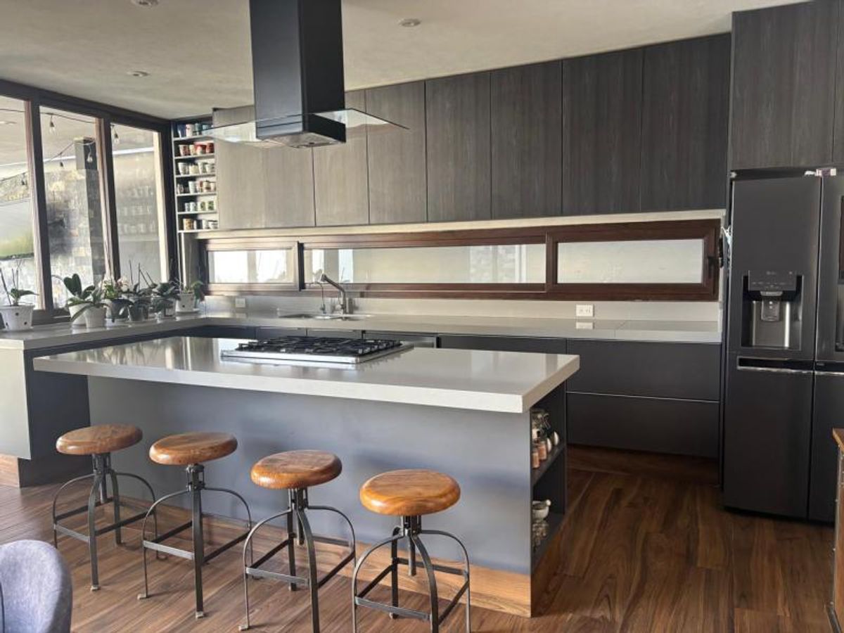 Cocina moderna con isla central, parrilla integrada, cuatro bancos de madera y gabinetes oscuros