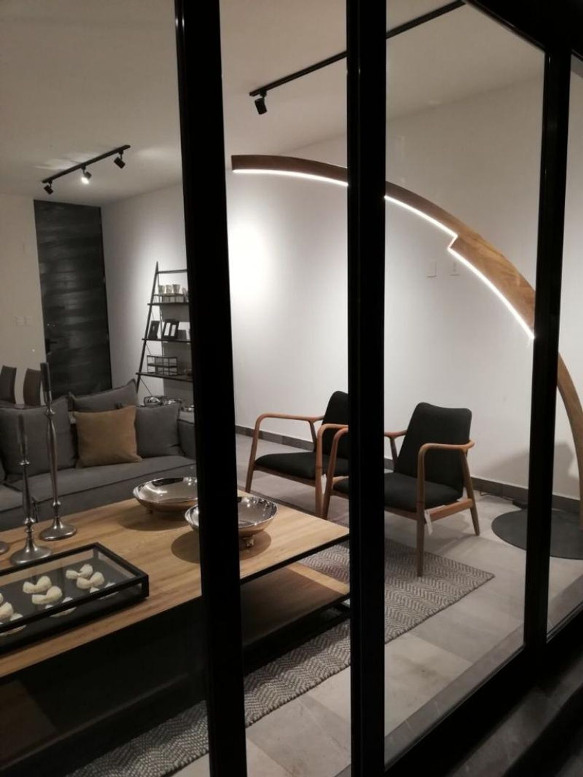 Sala de estar con mesa de madera, sillones oscuros y lámpara curva iluminada