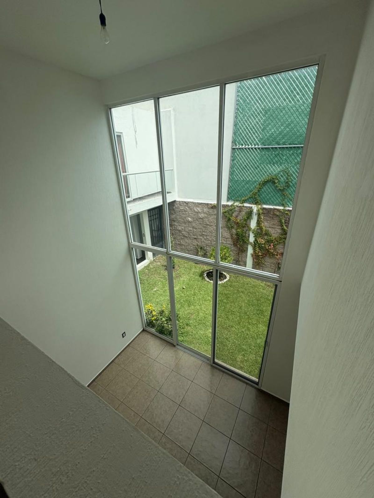 Espacio interior de doble altura con ventanales altos y vista hacia un jardín exterior