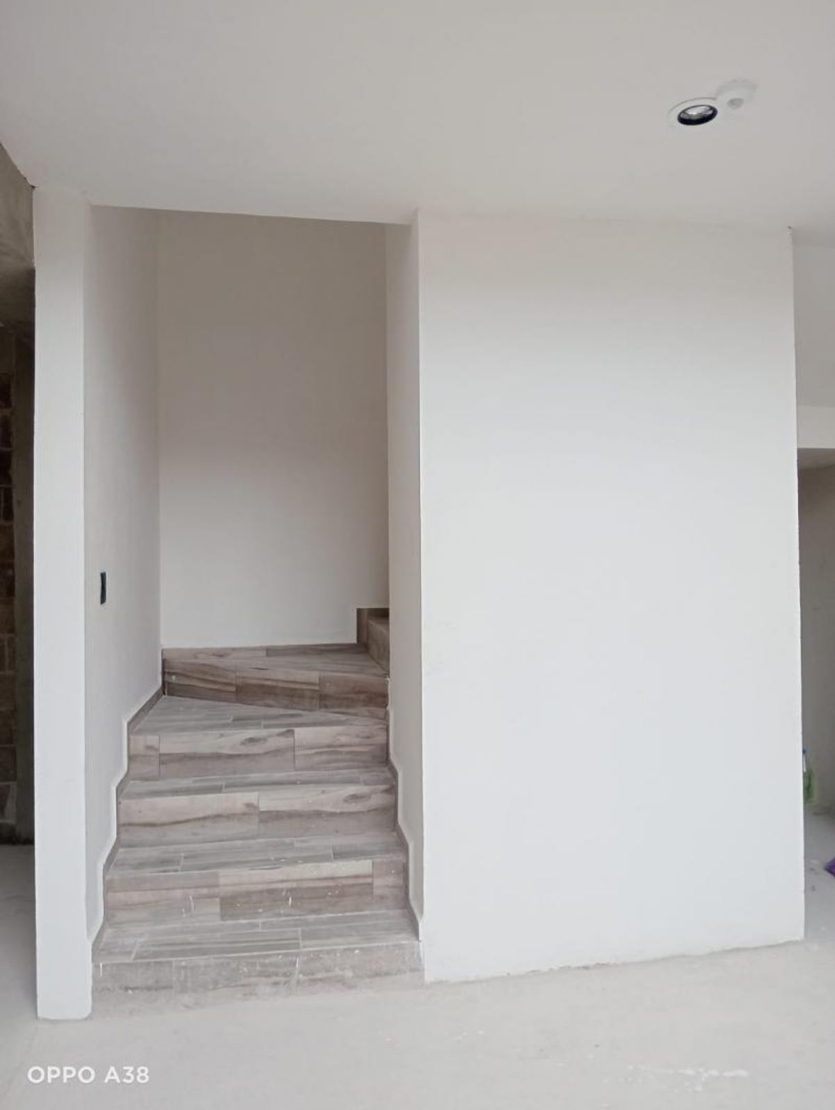Escalera interior con escalones cerámicos tipo madera, paredes blancas y luz empotrada en techo
