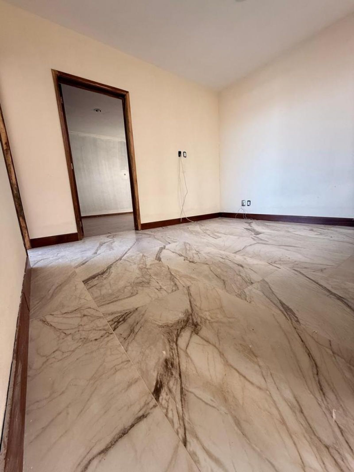 Habitación vacía con piso veteado estilo mármol, paredes claras y zócalo de madera oscura