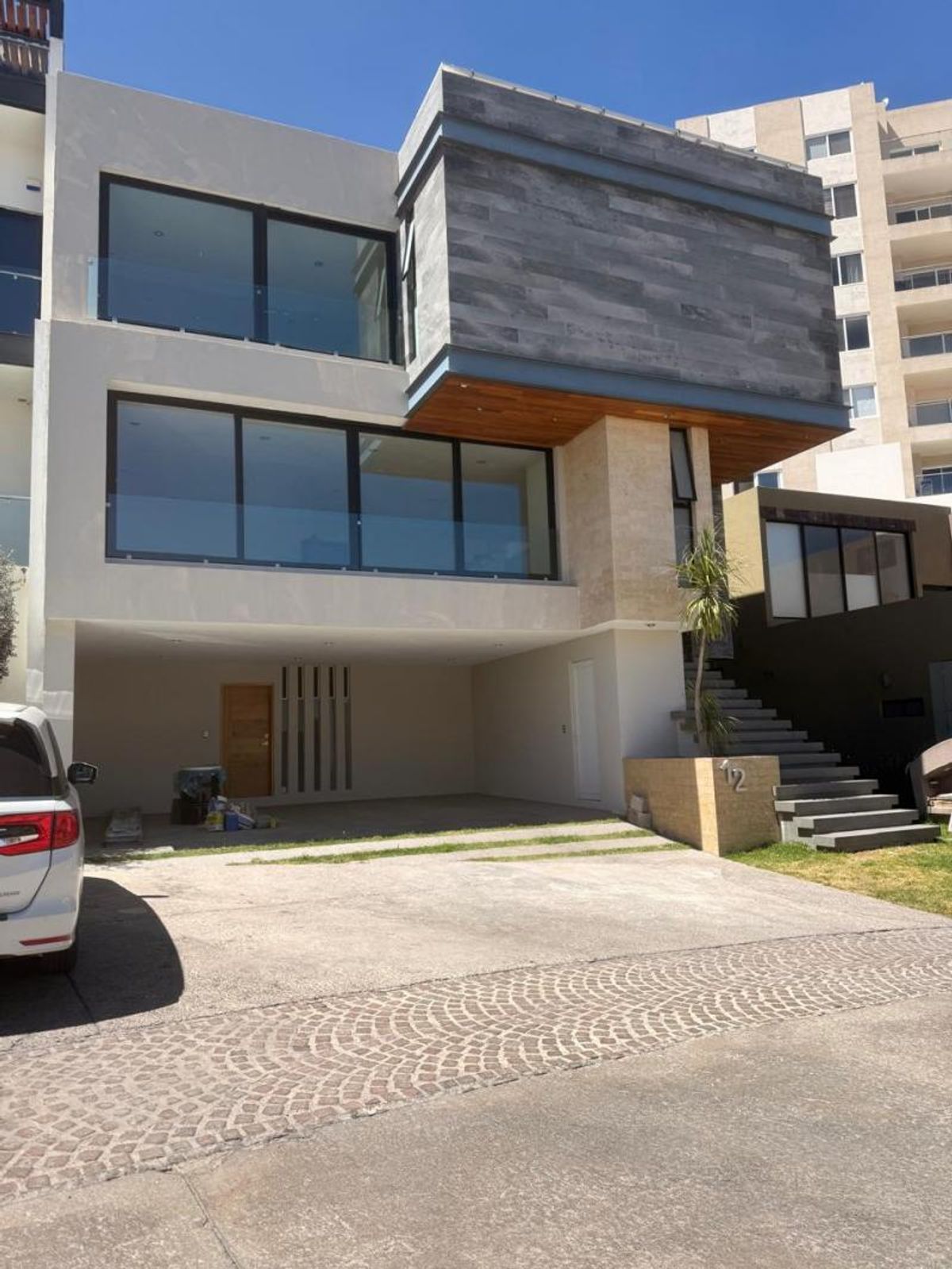 Fachada moderna con cochera abierta, grandes ventanales de cristal y revestimiento en piedra