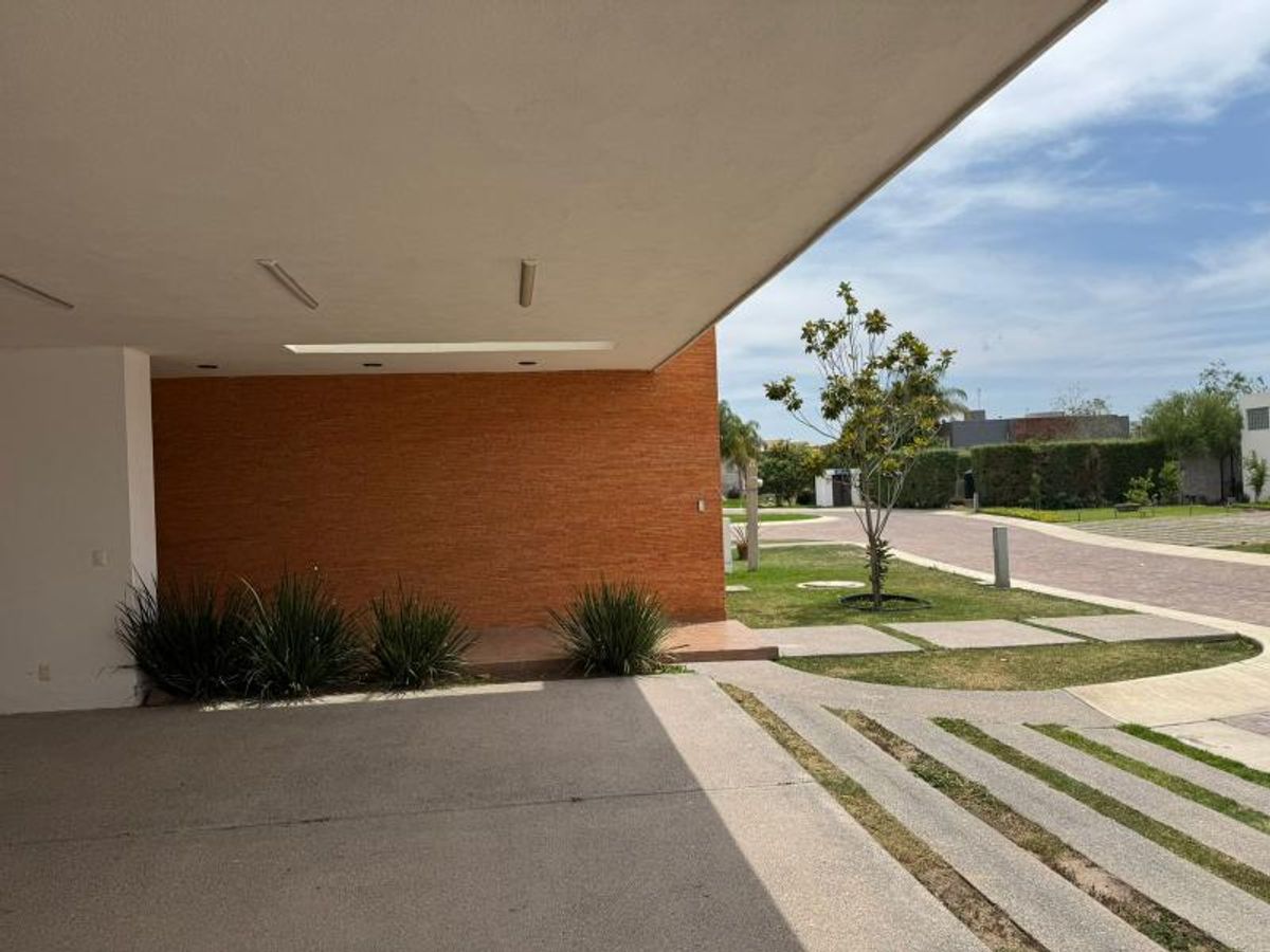 Cochera techada con muro texturizado terracota, plantas ornamentales y sendero de losas de concreto