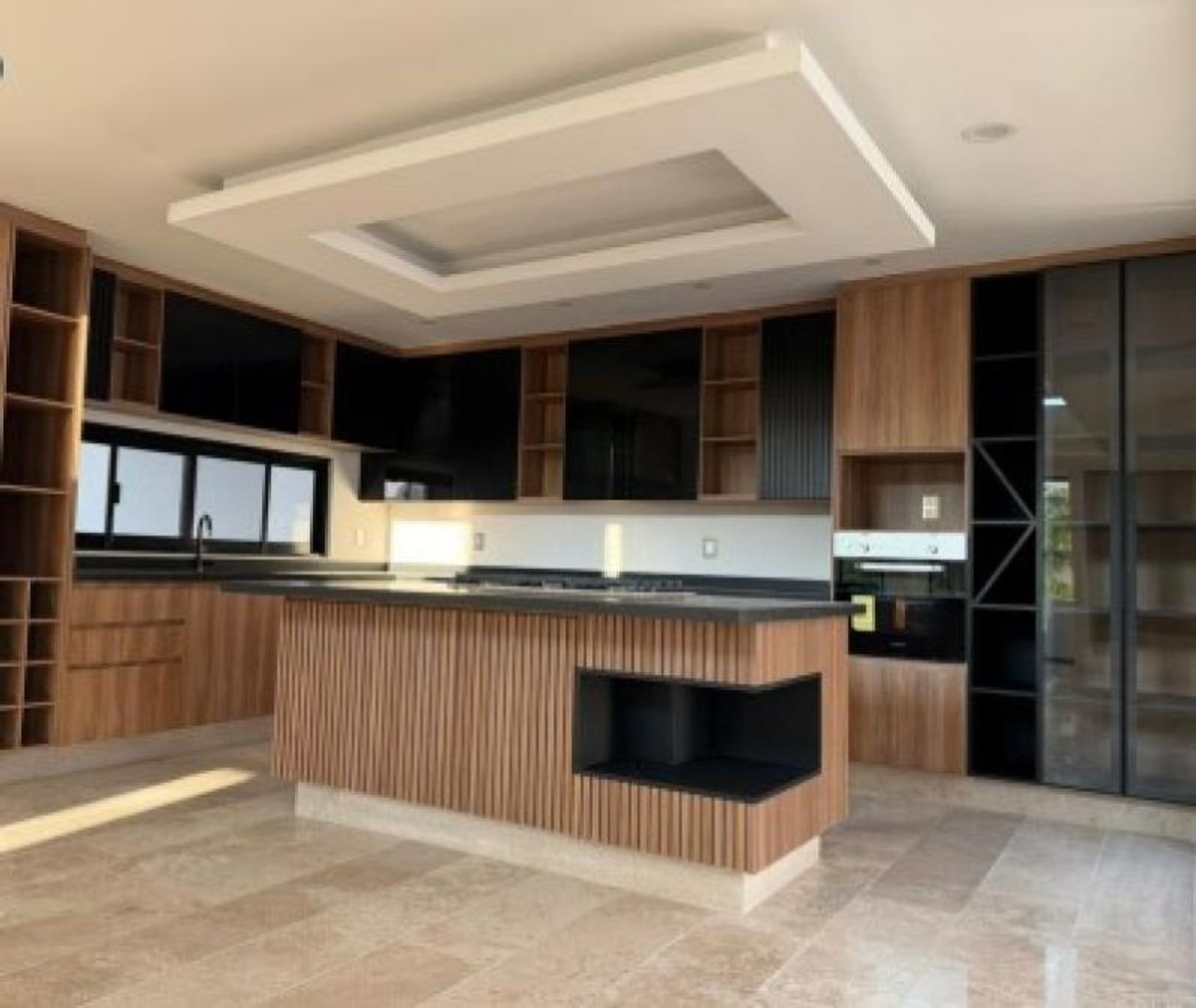 Cocina integral con isla de madera acanalada, gabinetes negros y piso de mármol
