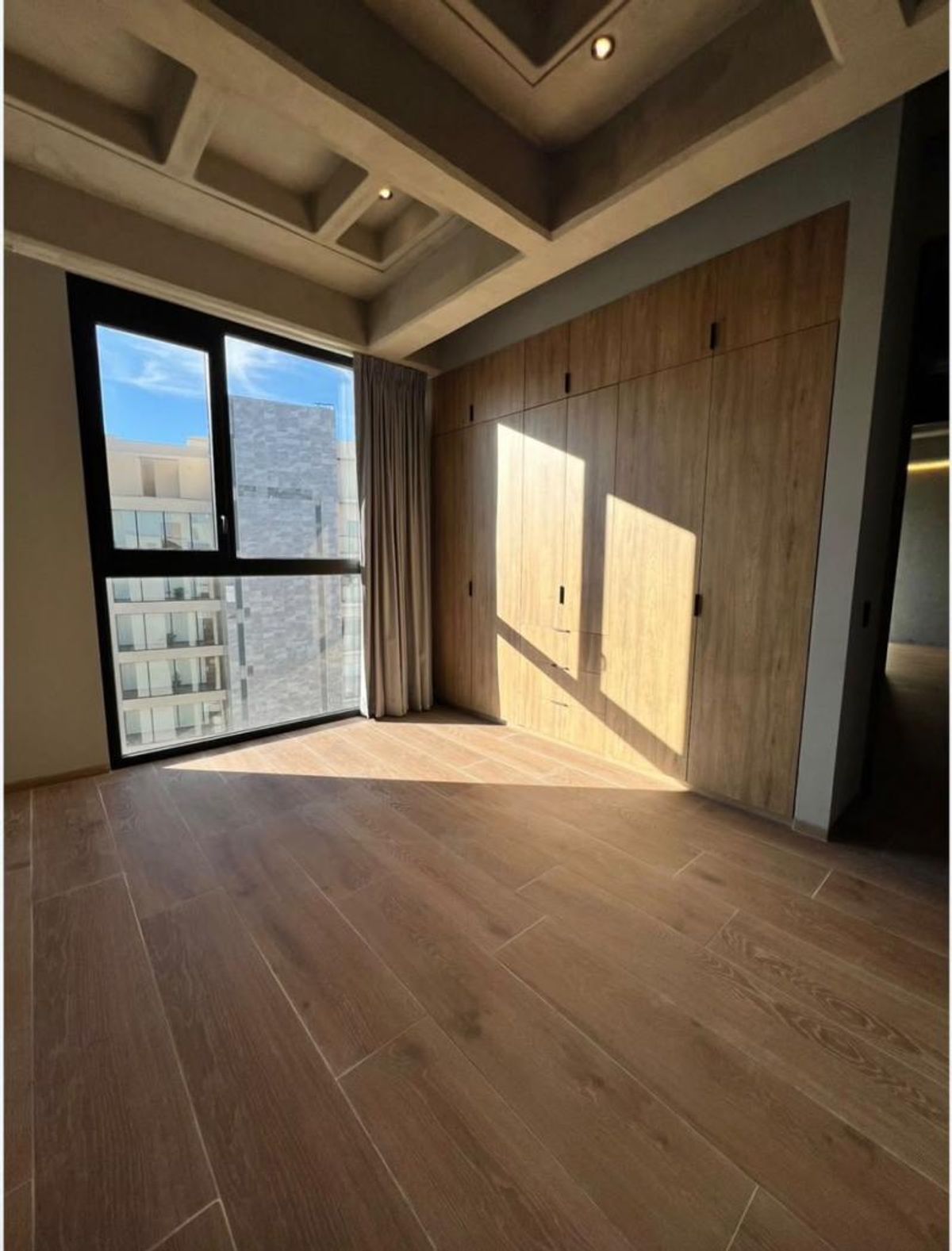 Recámara vacía con piso y clóset de madera, gran ventanal e iluminación natural
