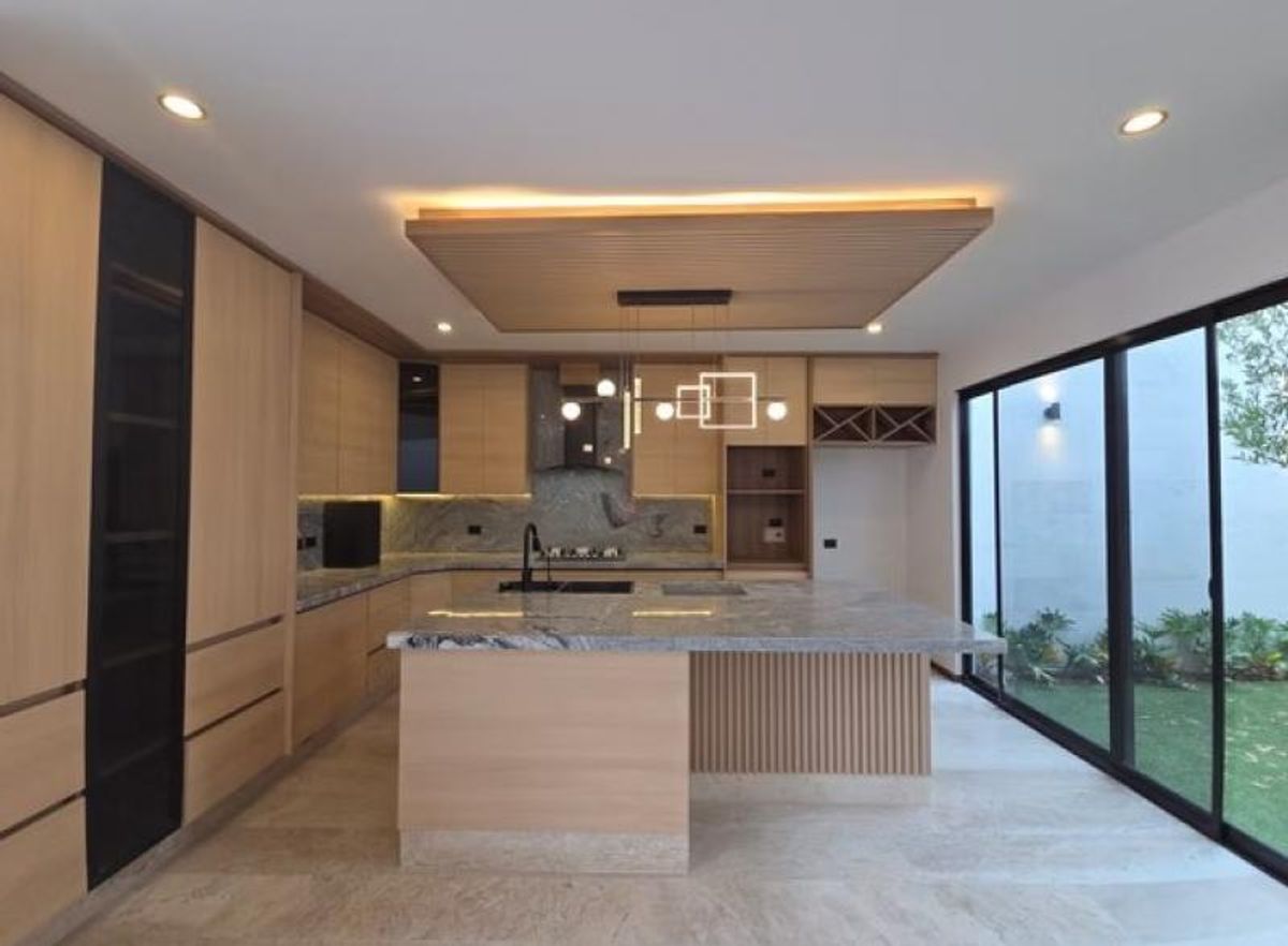 Cocina integral con isla de granito, gabinetes de madera y ventanales al jardín