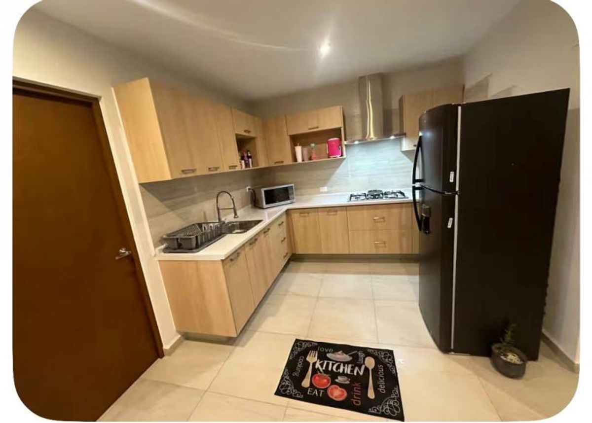 Cocina integral en L con gabinetes de madera clara, cubierta blanca y refrigerador negro