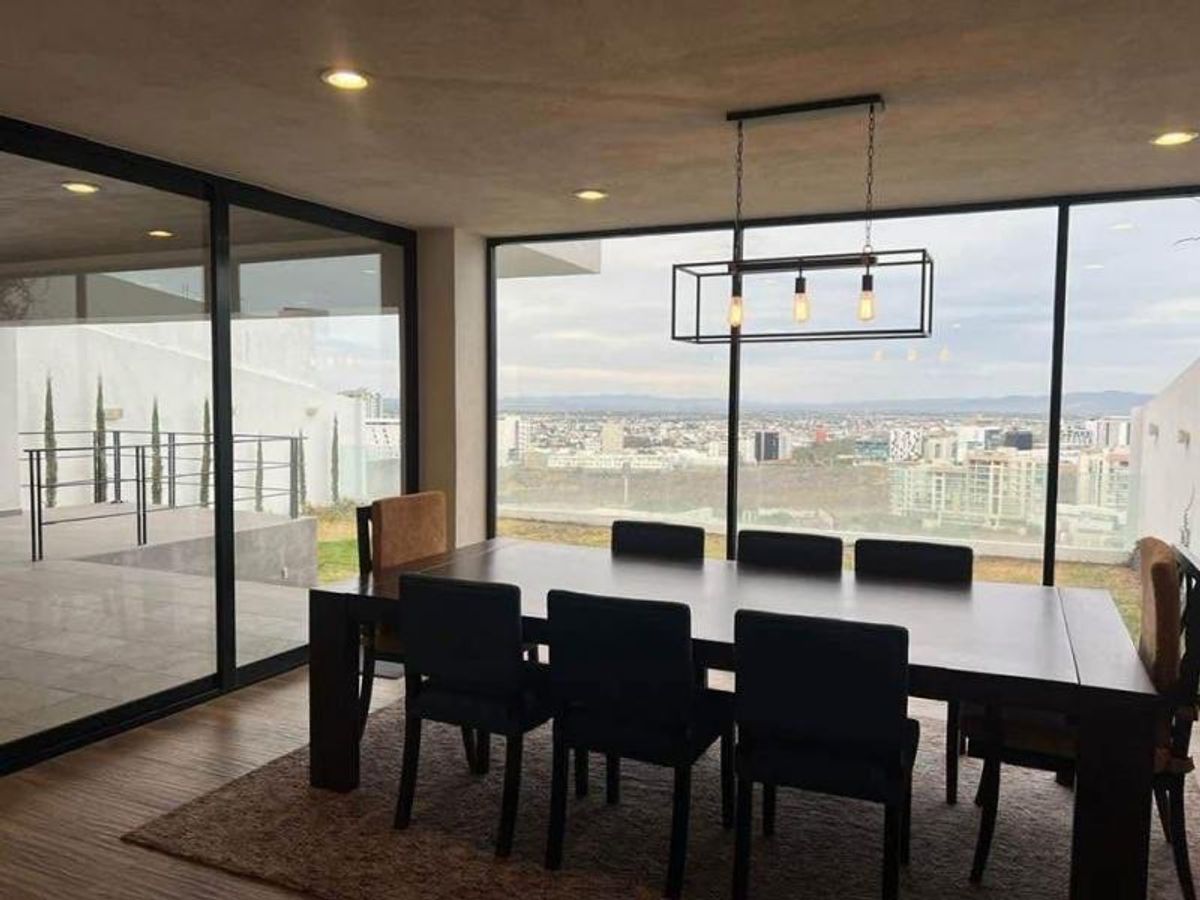 Comedor con mesa de madera, sillas negras, lámpara colgante y ventanales con vista panorámica