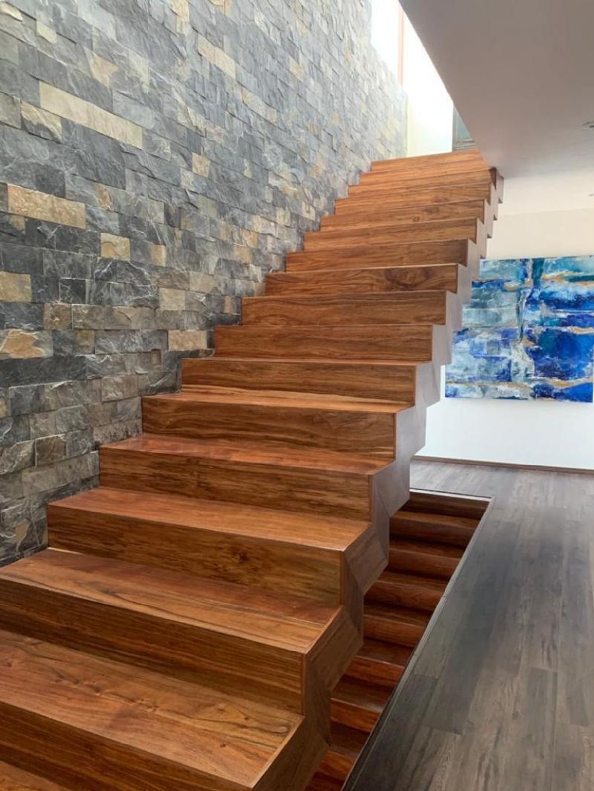 Escalera de madera con peldaños gruesos junto a un muro revestido de piedra