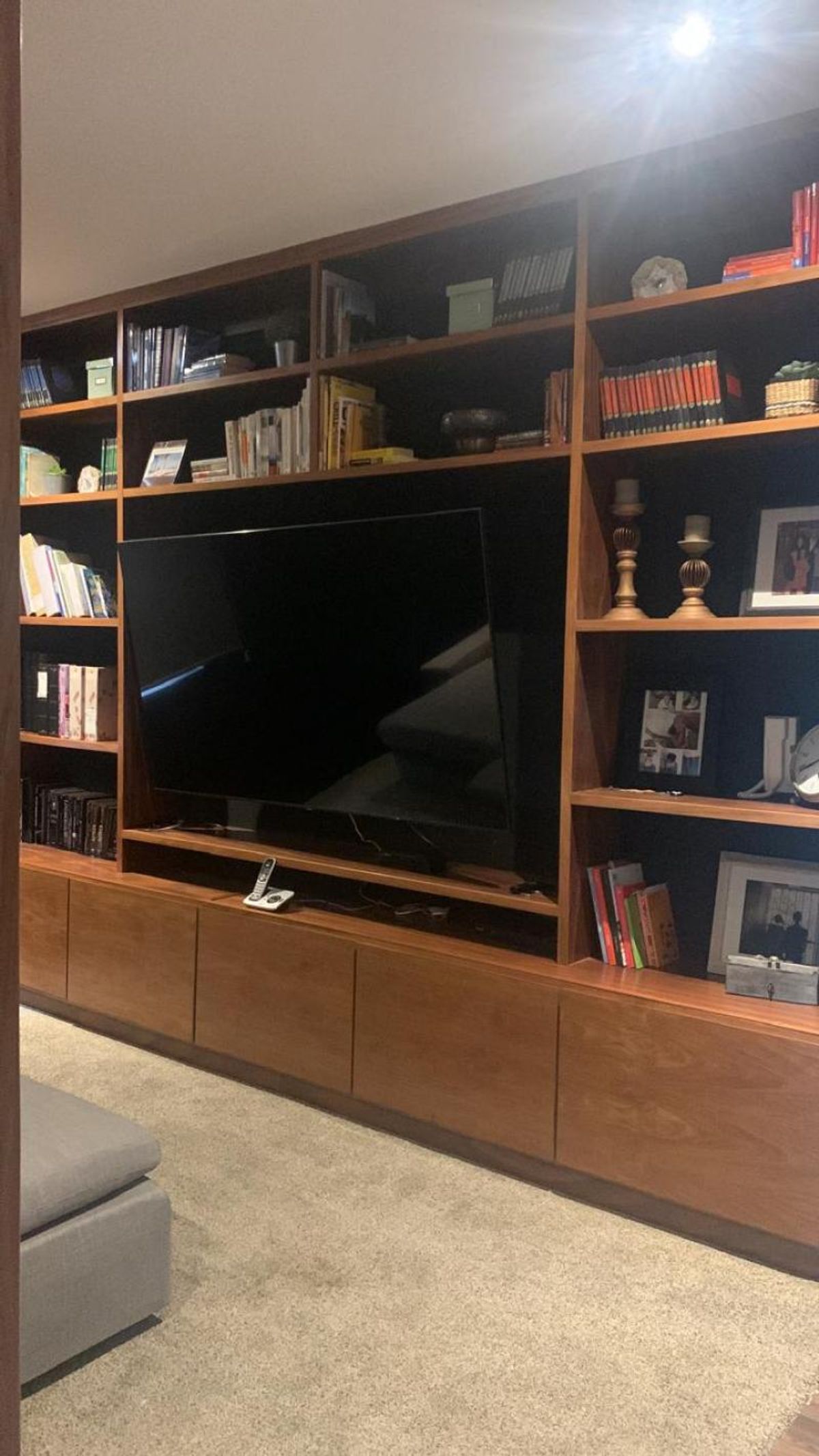 Mueble de madera empotrado con repisas, televisión al centro, gabinetes inferiores y piso alfombrado
