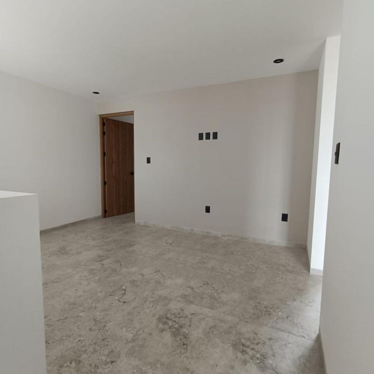 Habitación vacía con piso cerámico gris, paredes neutras, luces empotradas y puerta de madera